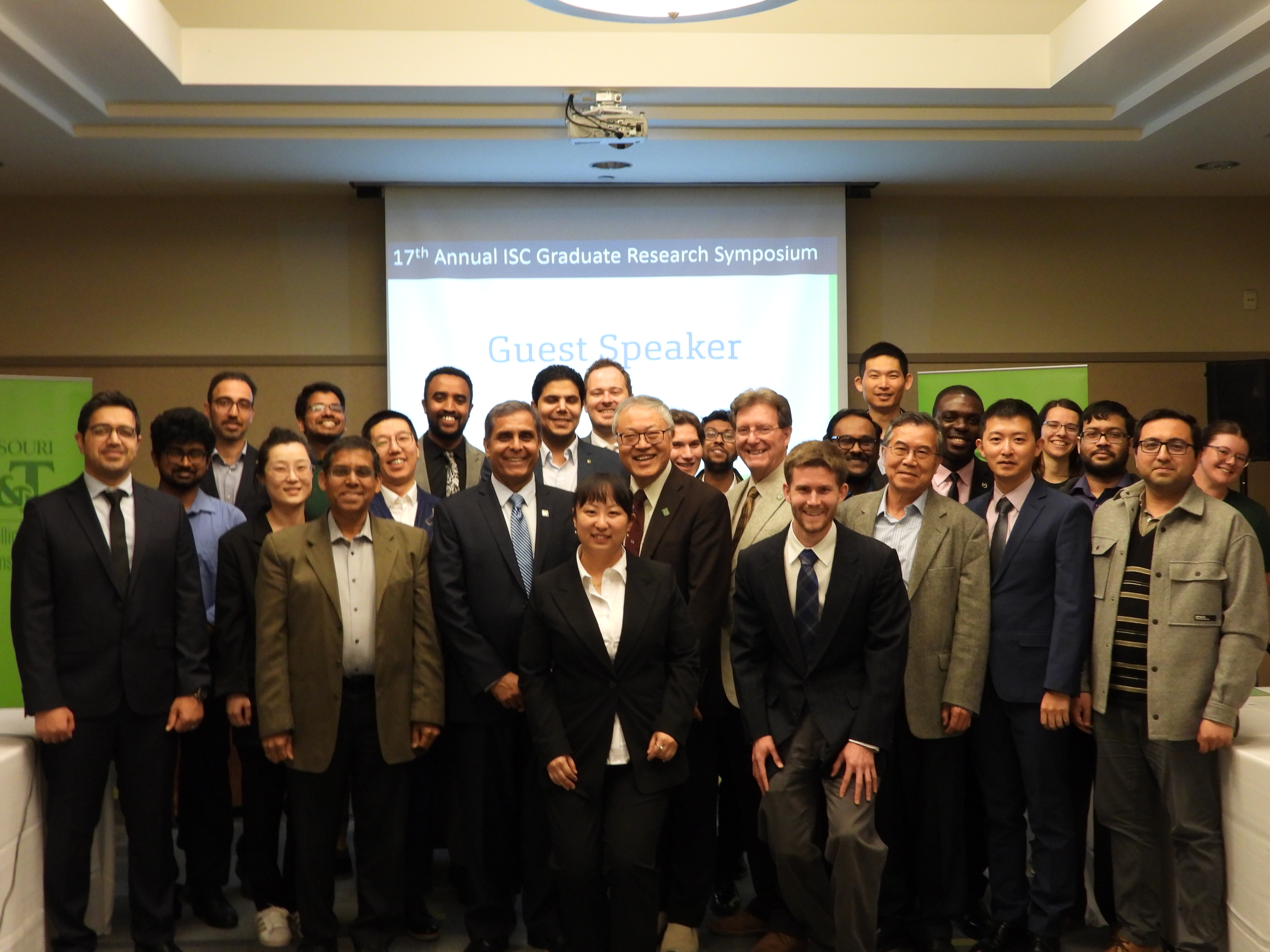 Group of students, judges, the chancellor, and guest speaker smiling at symposium event.